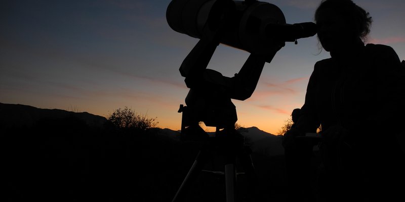 Frau am Teleskop vor Abendhimmel