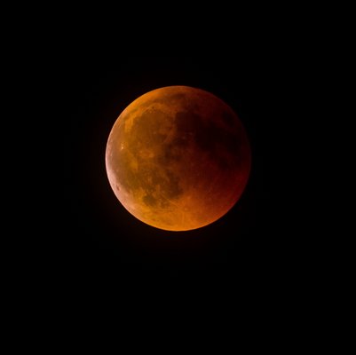 Fotografie eine Mondfinsternis. Der Vollmond wird durch in der Erdatmosphäre abgelenktes rötliches Sonnenlicht erhellt